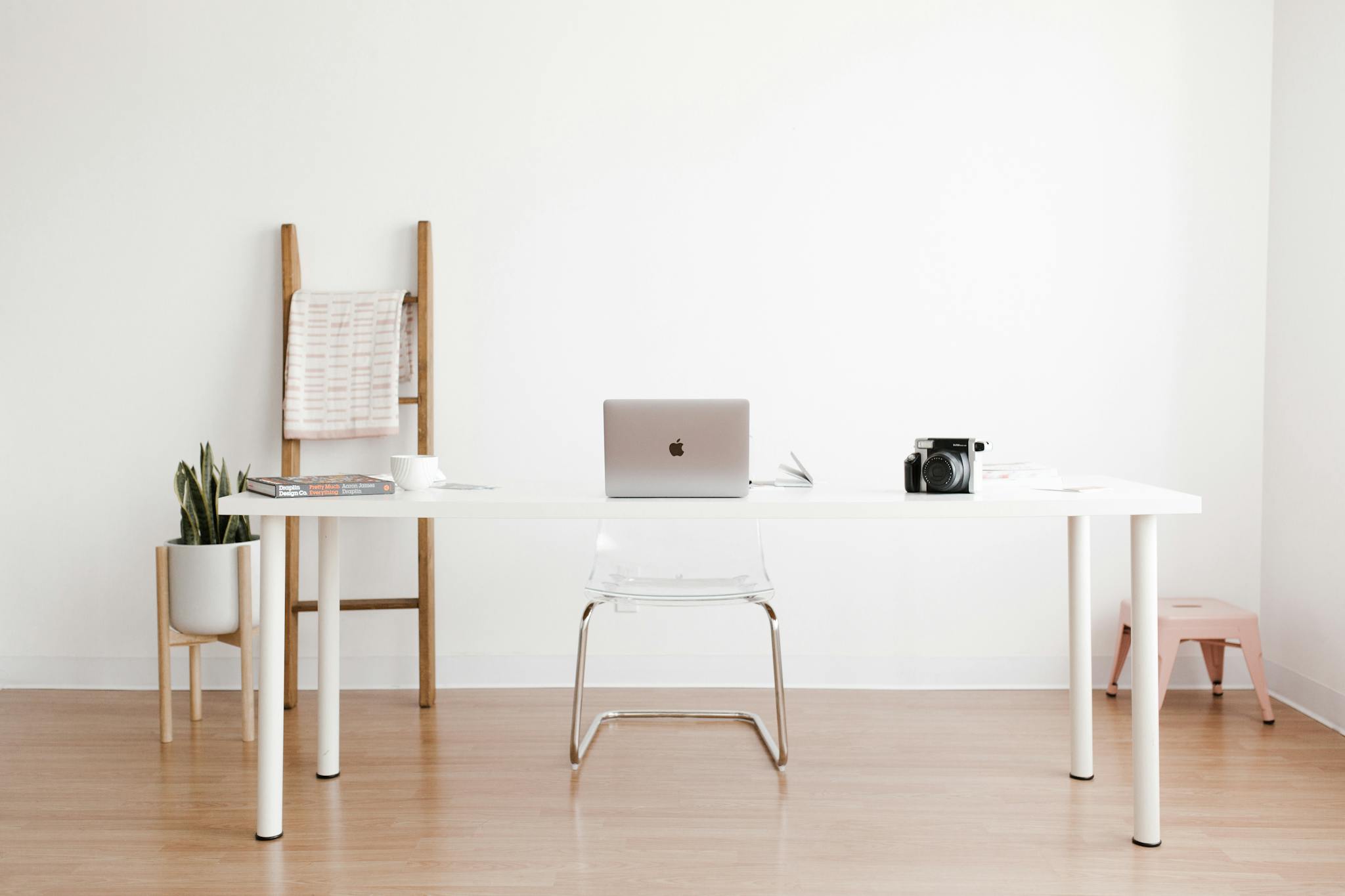 Bright and minimalist home office setup with a white desk, laptop, and potted plant.