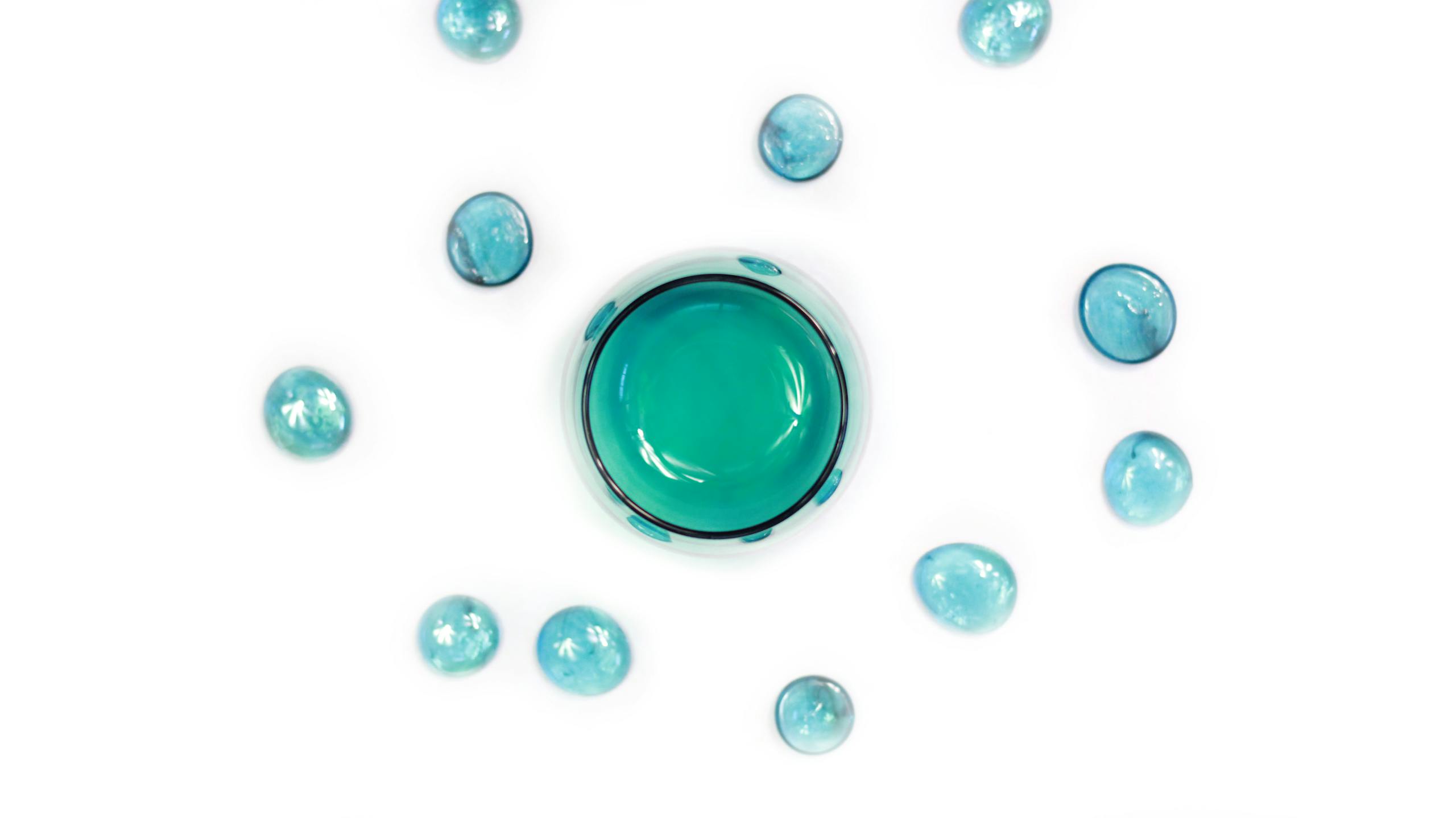 Minimalist arrangement of turquoise glass spheres with a central large sphere on a white background.